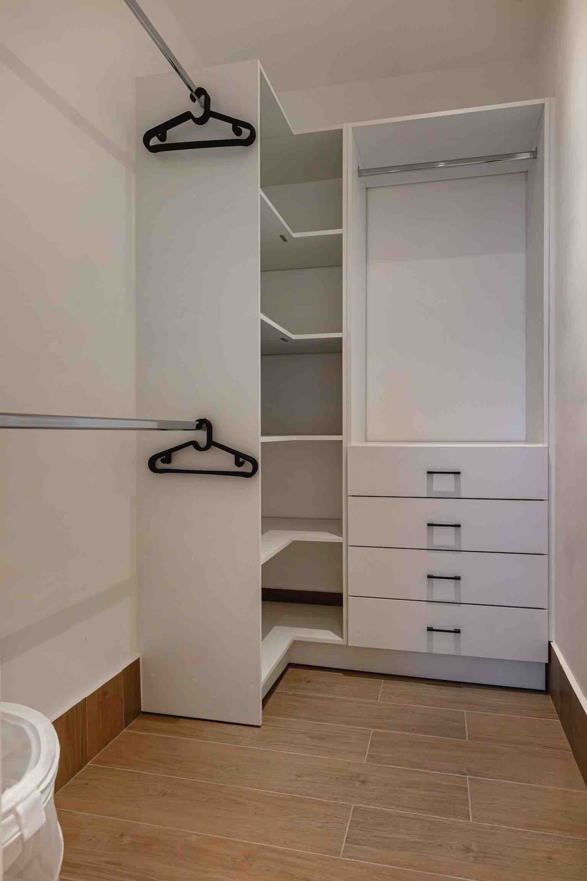 A walk-in closet with open doors, featuring multiple shelves and drawers, and two black hangers on the wall.