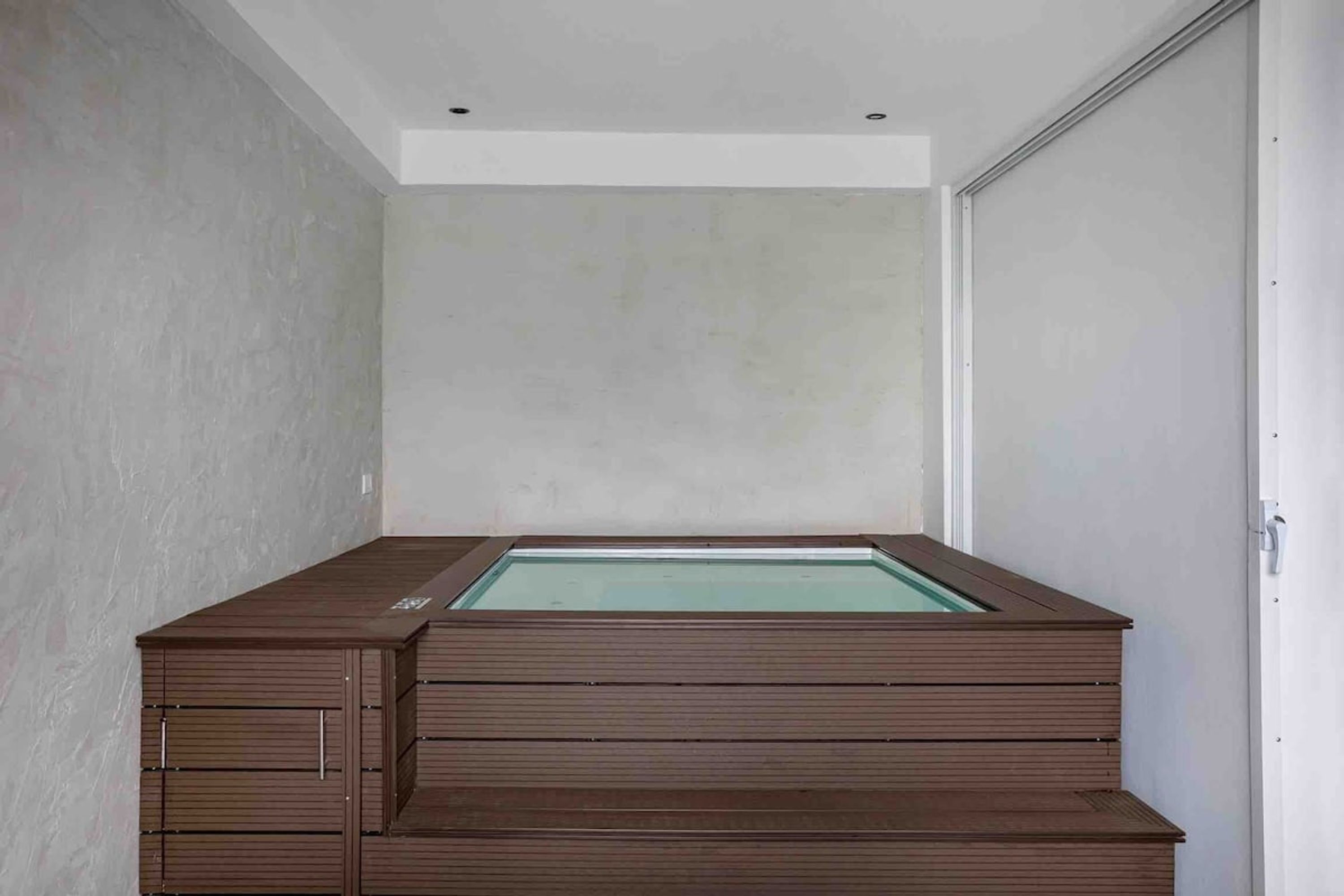 Une chambre moderne et minimaliste, dotée d’une baignoire en bois intégrée et d’une paroi de verre.