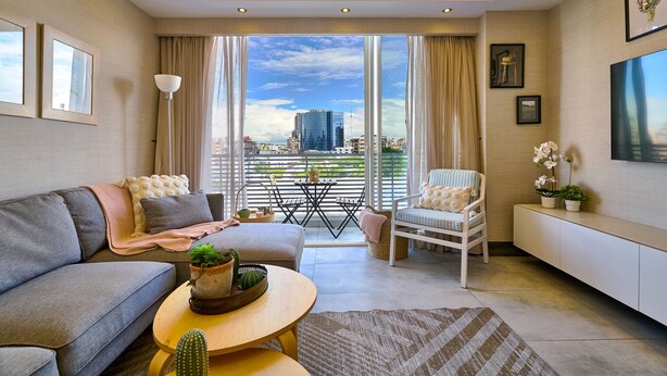 A modern living room with a sofa, armchair, and coffee table, large windows with a city view, and a flat-screen TV on the wall. - Piantini Views Downtown SD Gym Lounge Pool (Santo Domingo)