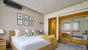 A bedroom with a large bed, bedside tables, a wall-mounted air conditioner, and framed botanical prints. - Piantini Views Downtown SD Gym Lounge Pool (Santo Domingo)