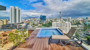 A rooftop pool with wooden deck and lounge chairs, overlooking a cityscape with modern buildings. - Piantini Views Downtown SD Gym Lounge Pool (Santo Domingo)