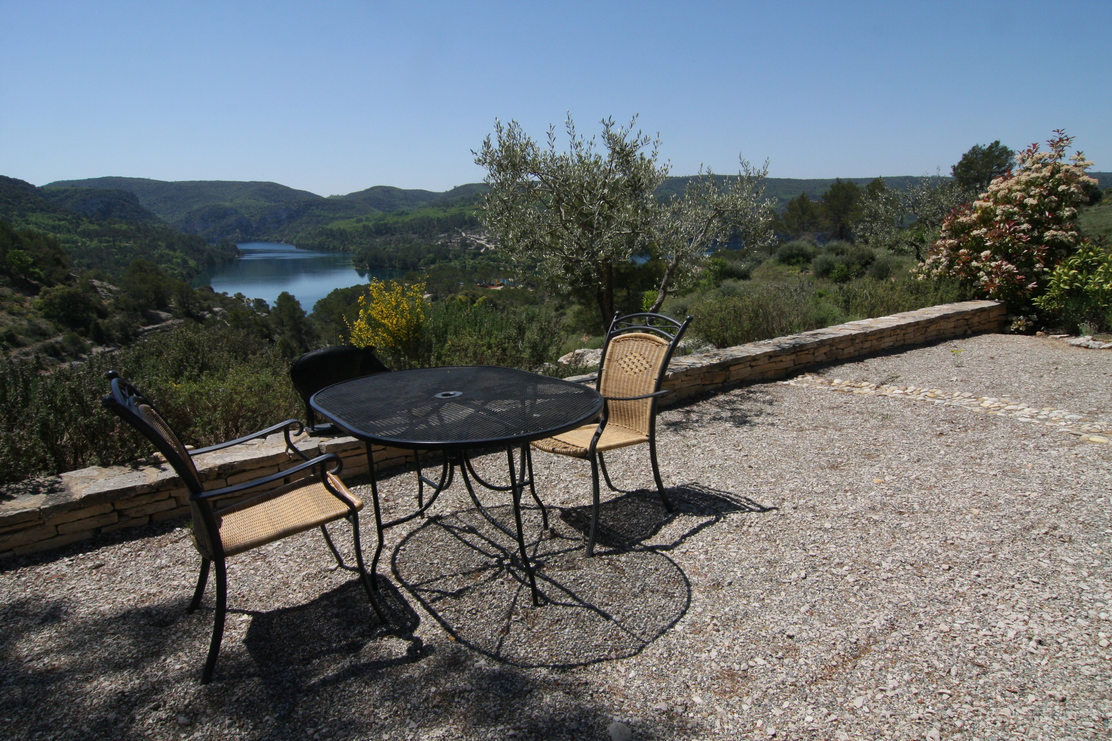 Een terras met een tafel en stoelen, met uitzicht op een meer en heuvels.