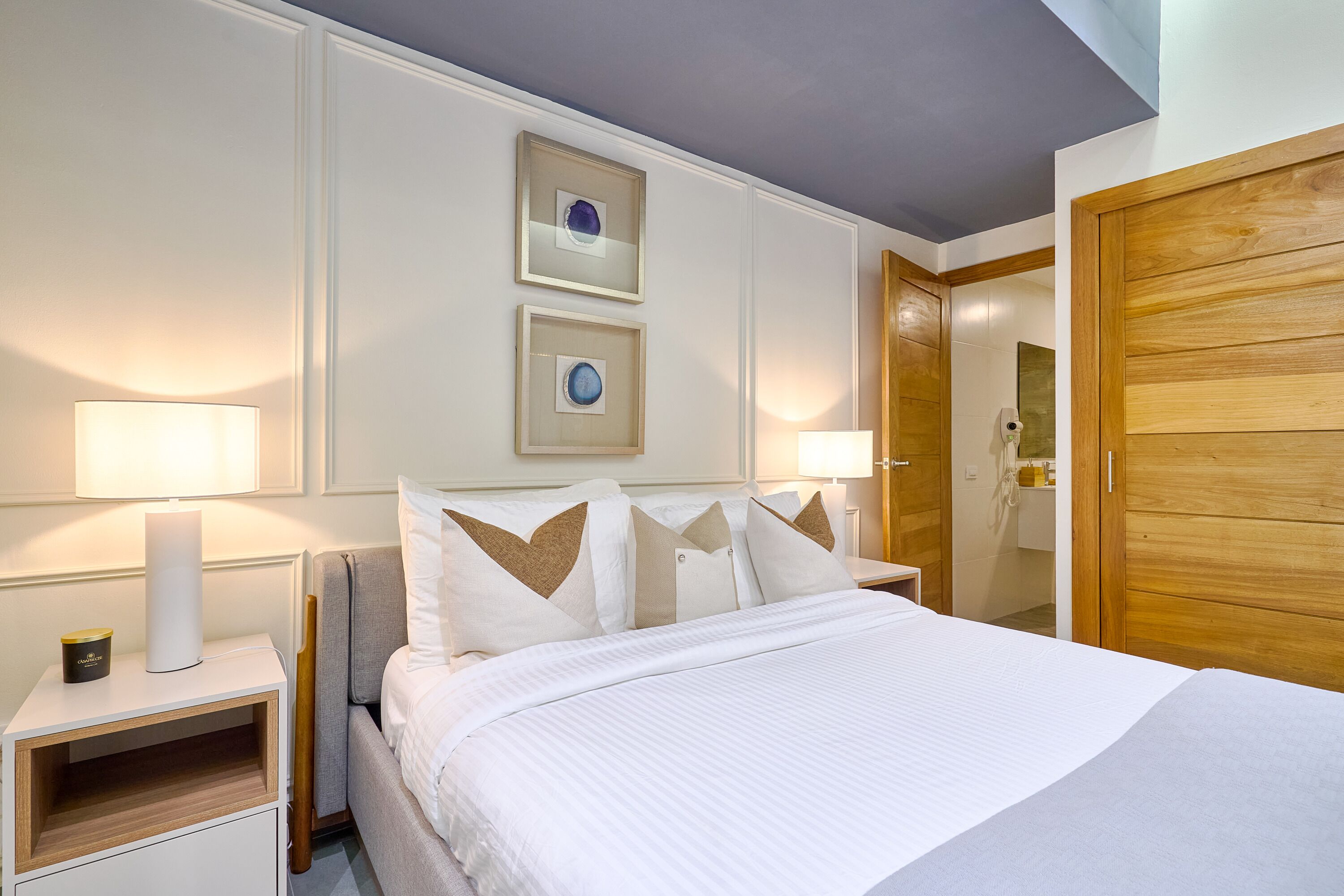 A neatly arranged bedroom with a bed, bedside lamps, a nightstand, and a wooden wardrobe.