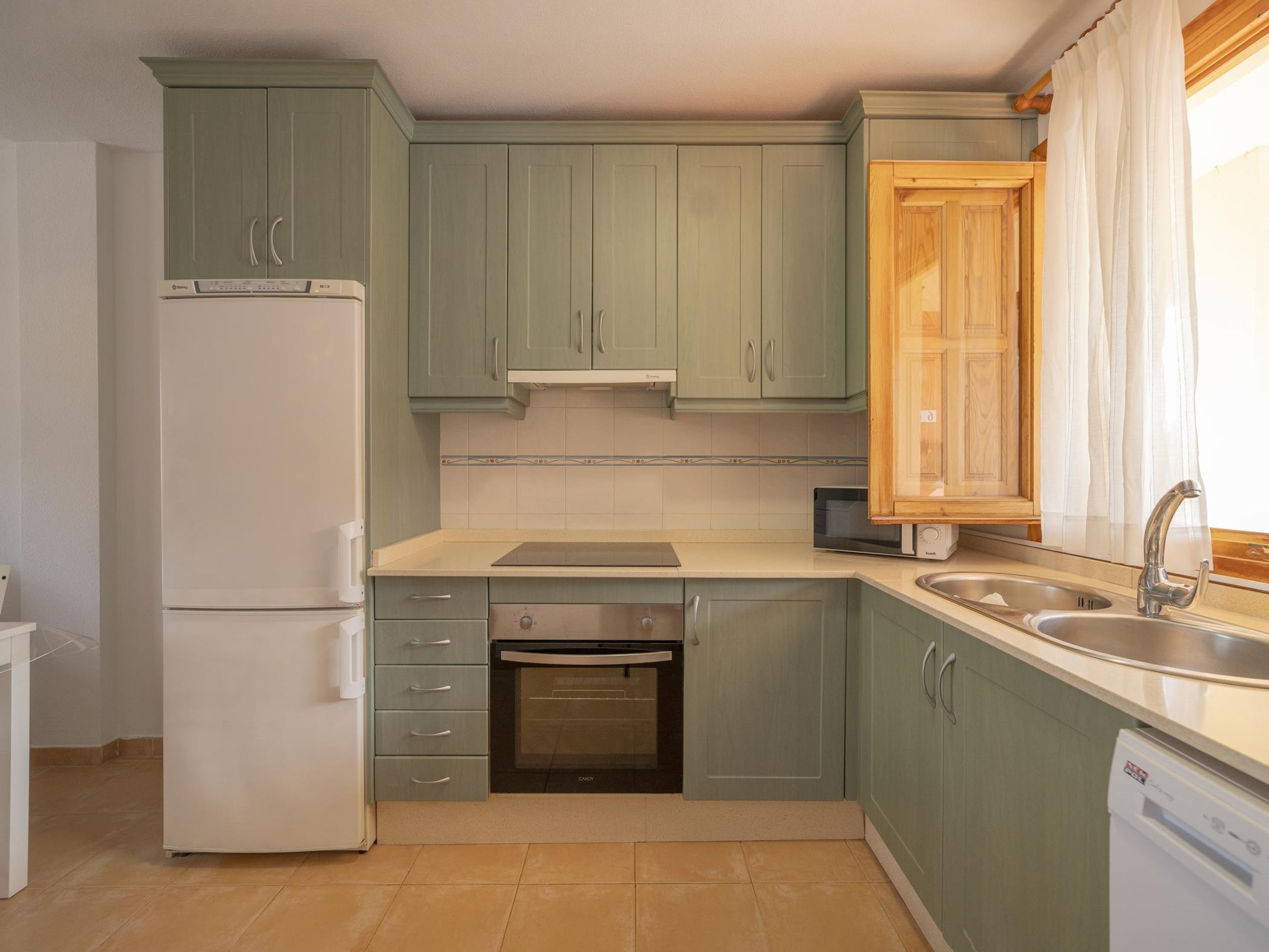 A kitchen with light green cabinets, a white refrigerator, a dishwasher, and a microwave.