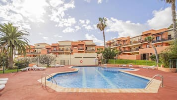 A swimming pool surrounded by a red brick patio, with a multi-story building in the background.
