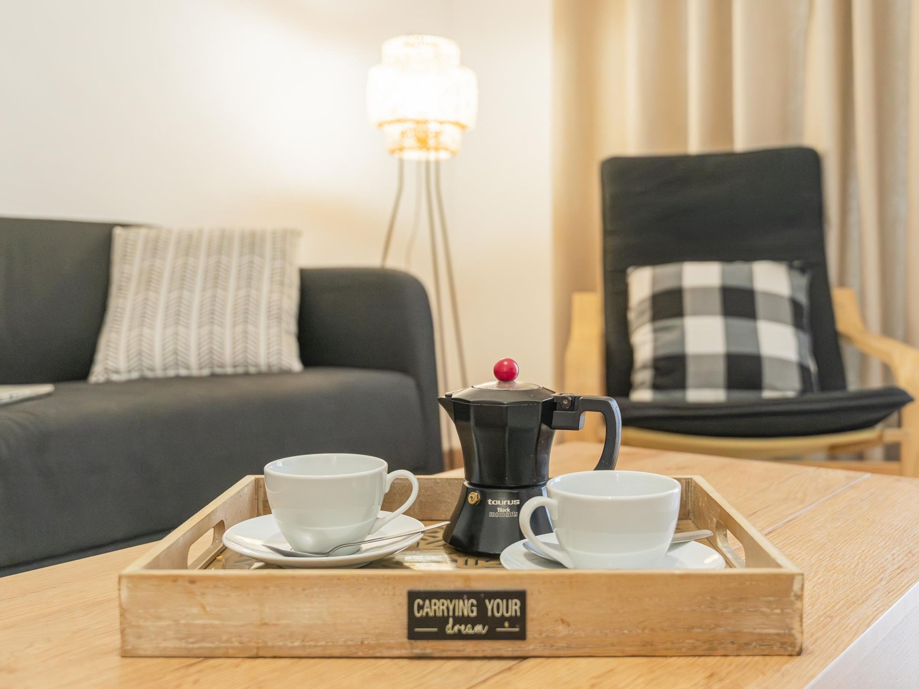 A wooden tray with two white cups and a coffee maker on a table.