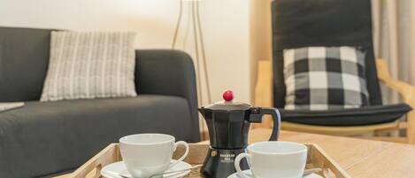 A wooden tray with two white cups and a coffee maker on a table.