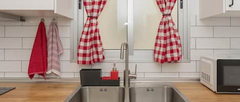 A modern kitchen with two stainless steel sinks, a microwave, and red and white checkered curtains.
