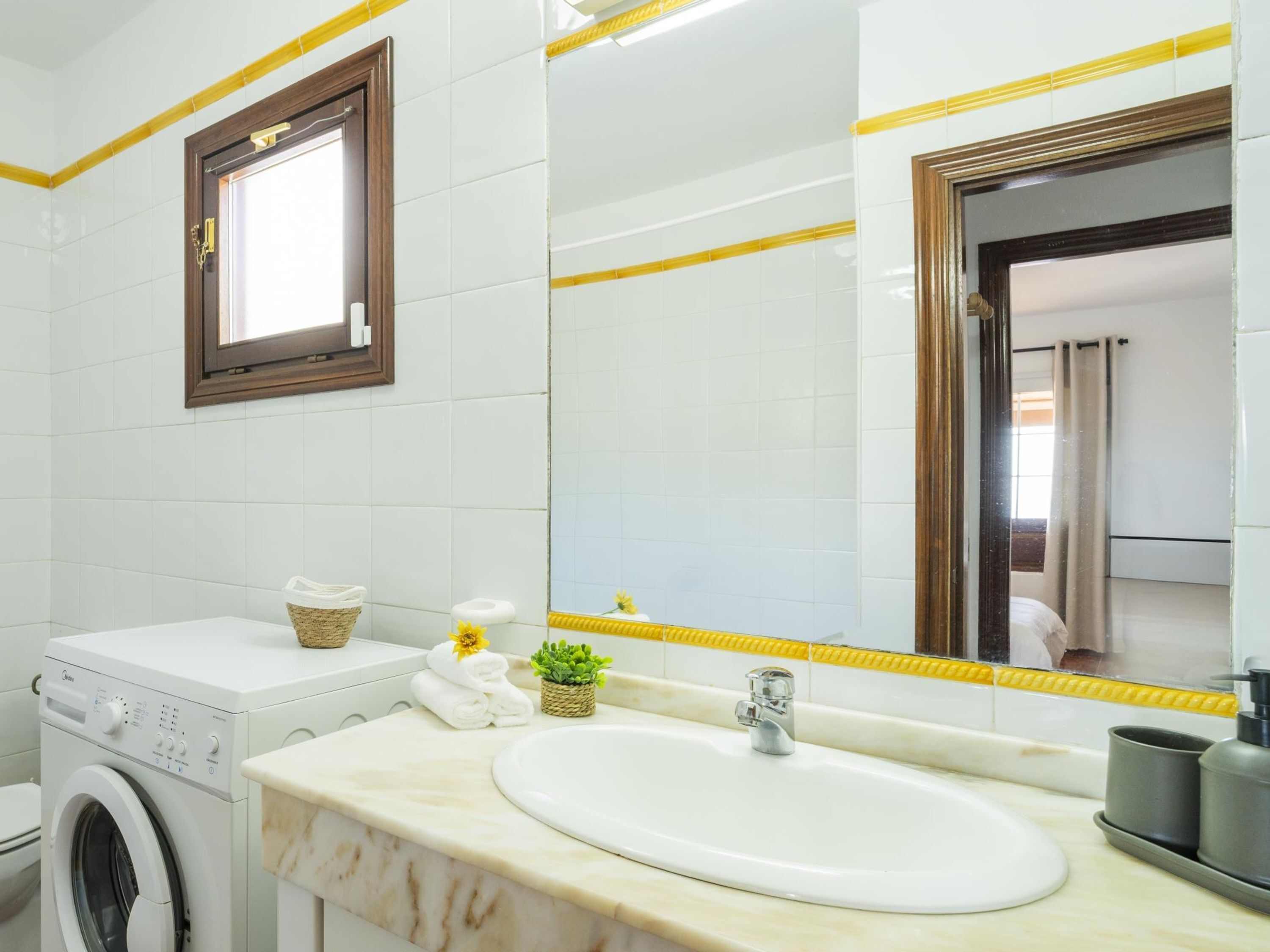A modern bathroom with a built-in washing machine, a sink with a marble countertop, and a large mirror with yellow accents.