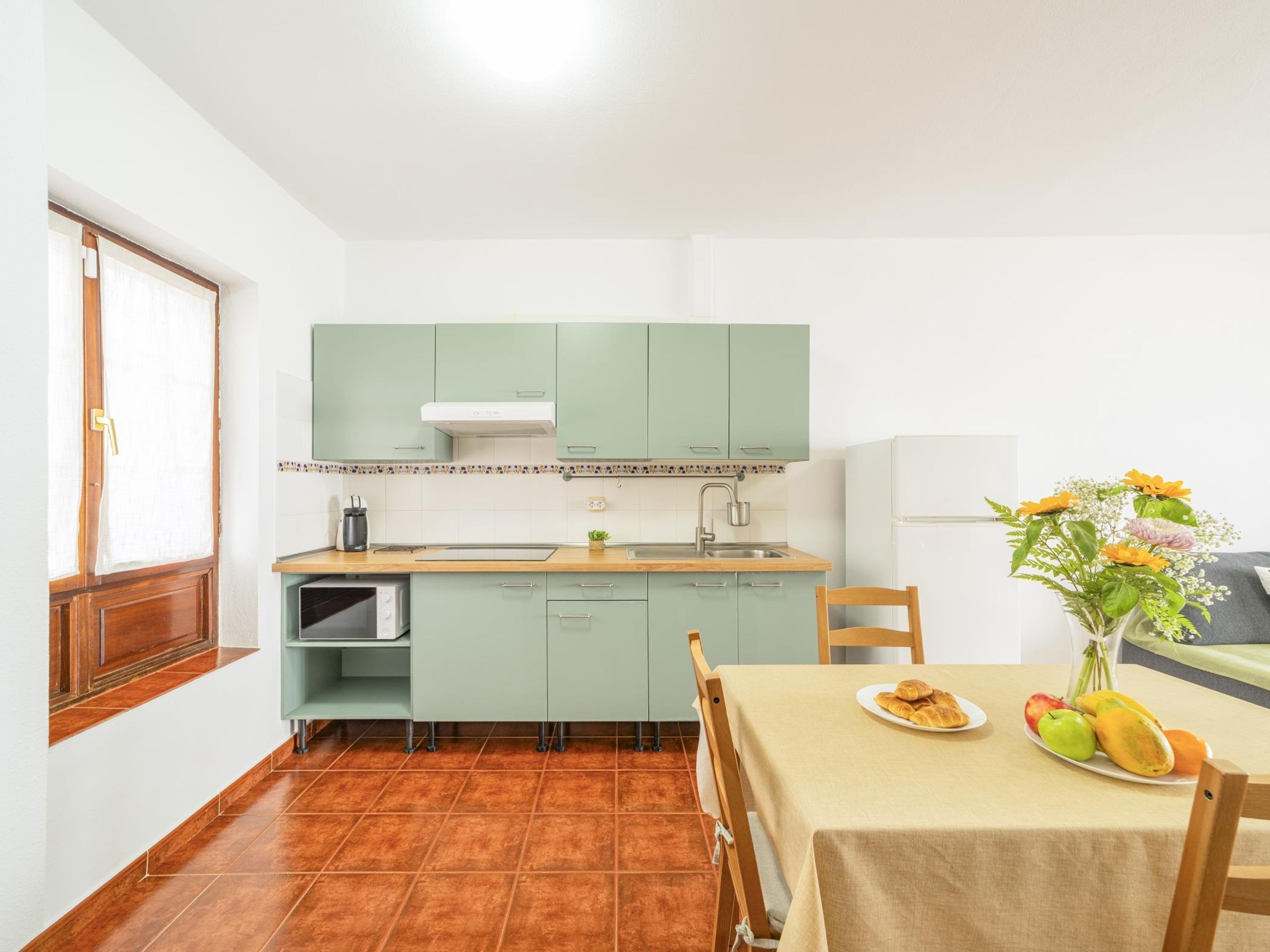 A compact kitchen with teal cabinets, a white stove, and a dining area with a table set for two.