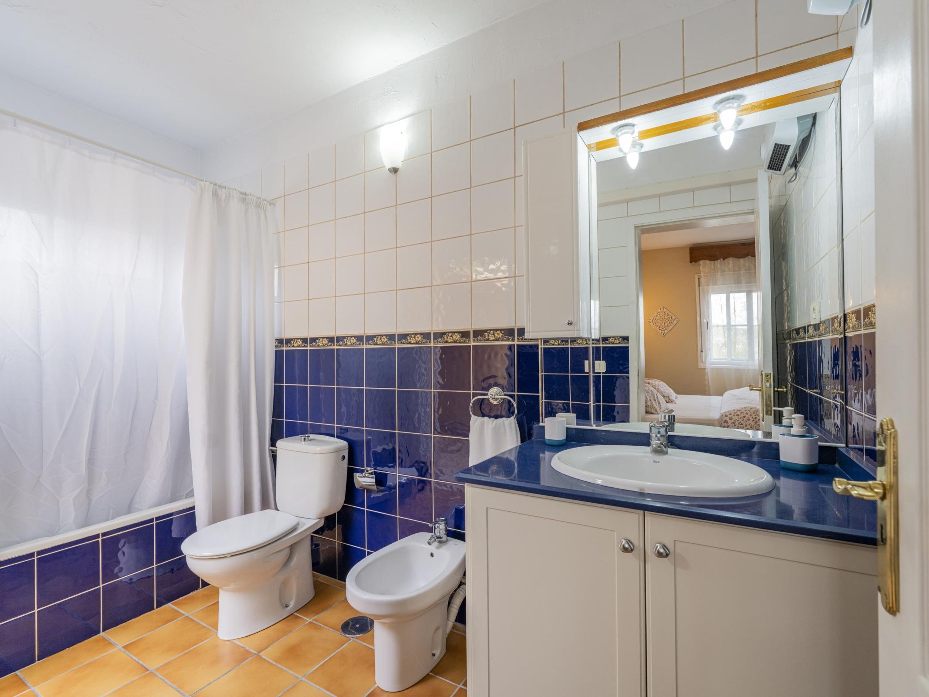 Un baño con inodoro, bidé, lavamanos y espejo.
