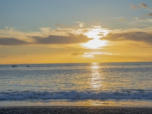 Et strandbillede med solnedgang over havet, både i det fjerne og bølger der nærmer sig kysten.