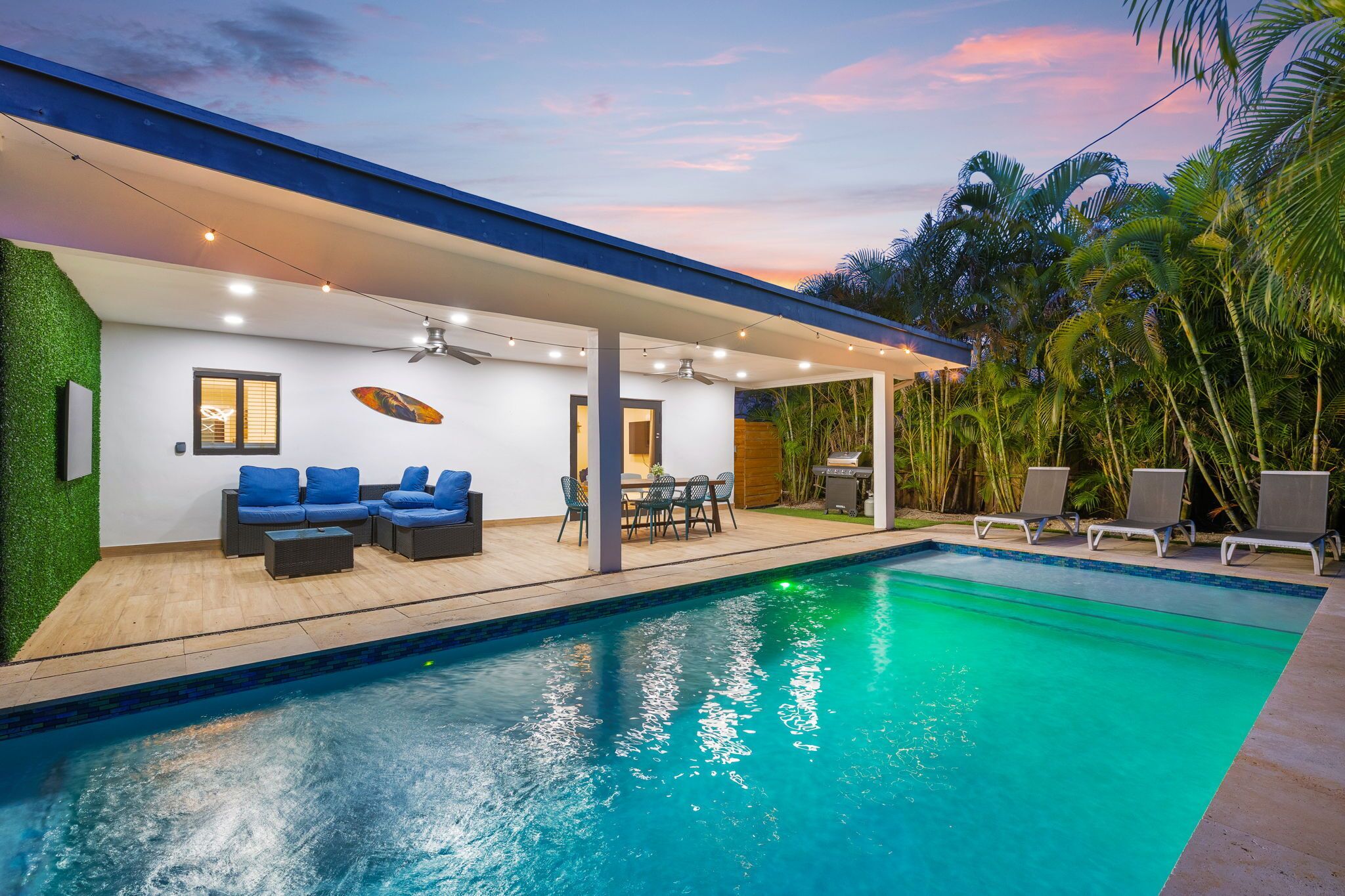 A modern poolside area with a covered seating area, a pool, and surrounding greenery.