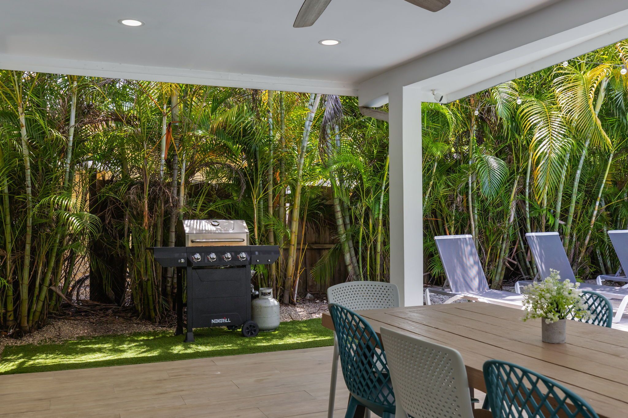 A covered patio with a grill, outdoor seating, and lush tropical vegetation.