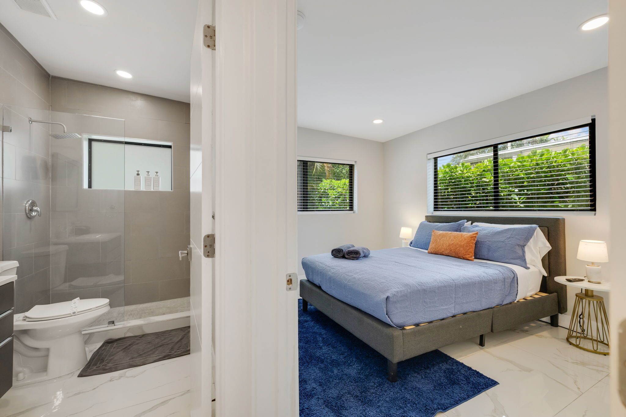 A modern bedroom with a bed, bedside table, and a window with blinds.