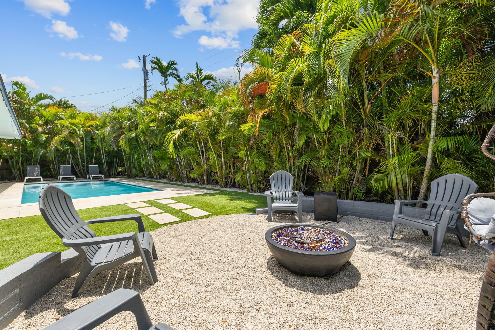 A poolside area with a fire pit, lounge chairs, and a view of a swimming pool surrounded by lush greenery.