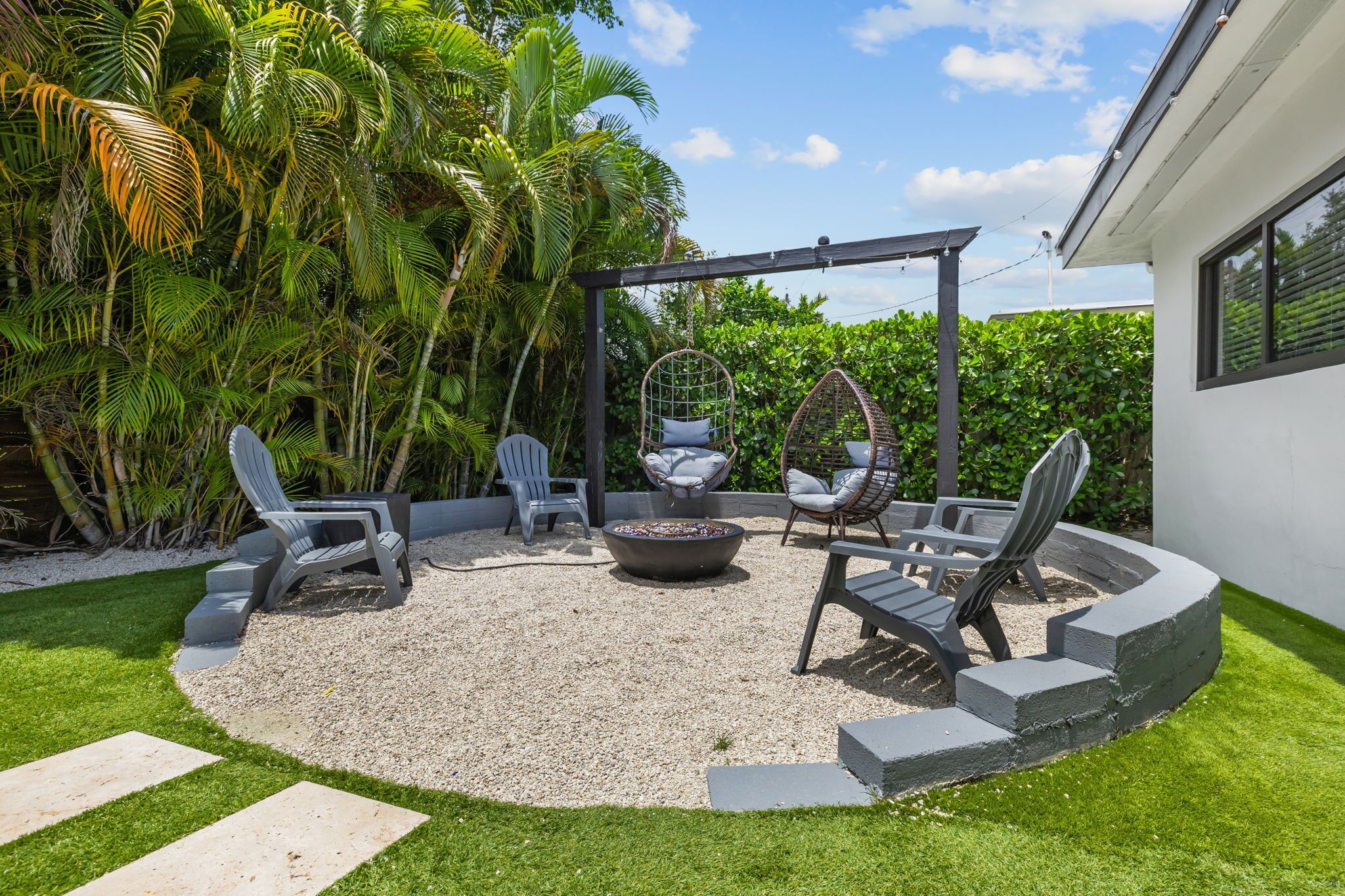 A circular outdoor seating area with chairs, a fire pit, and a pergola.