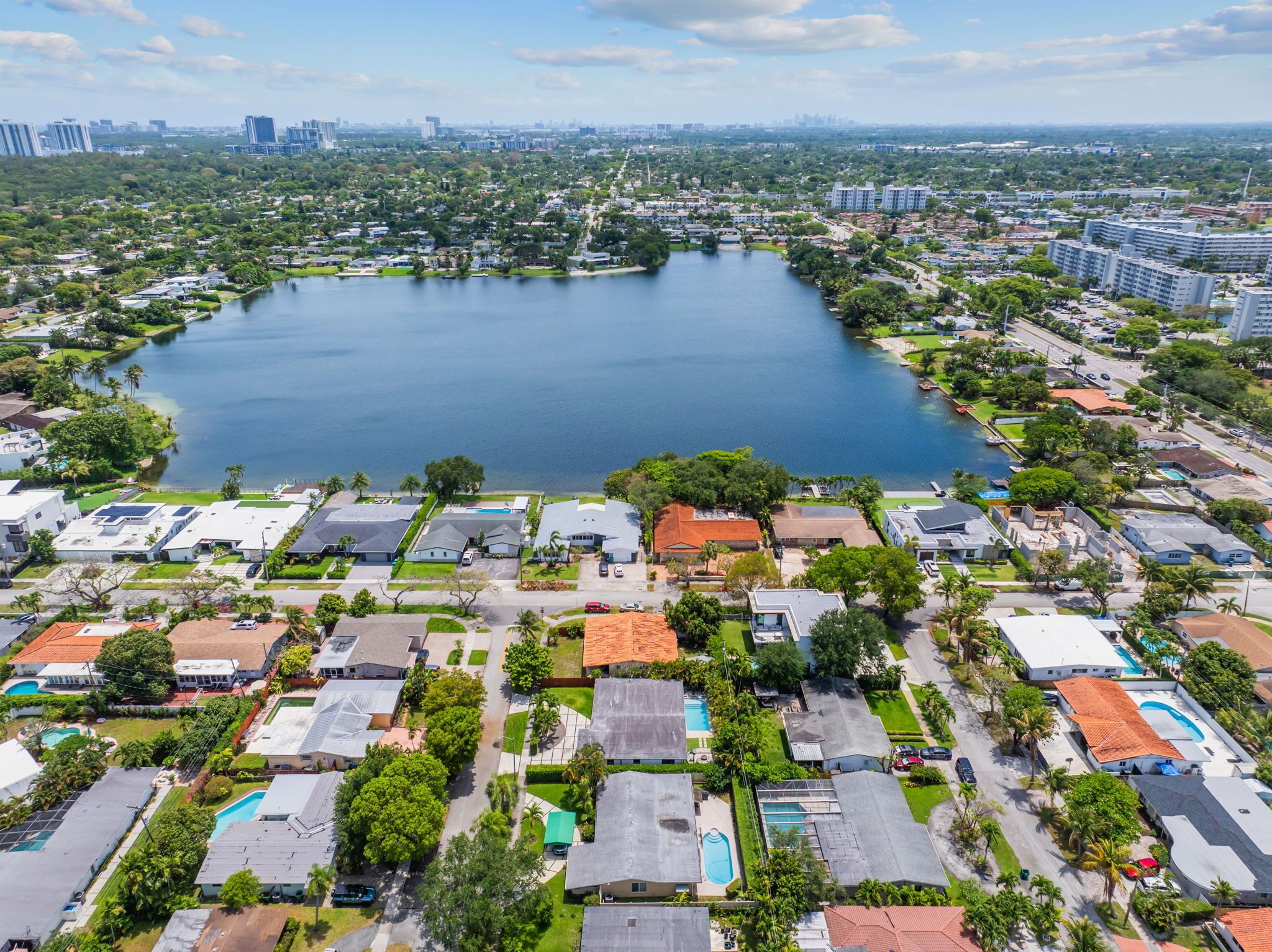 An aerial view of a residential area with a large lake surrounded by houses, some with visible swimming pools.