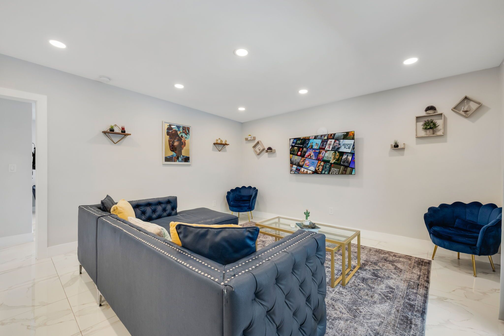 A modern living room with a grey sofa, a blue armchair, a glass coffee table, and a wall art collage.