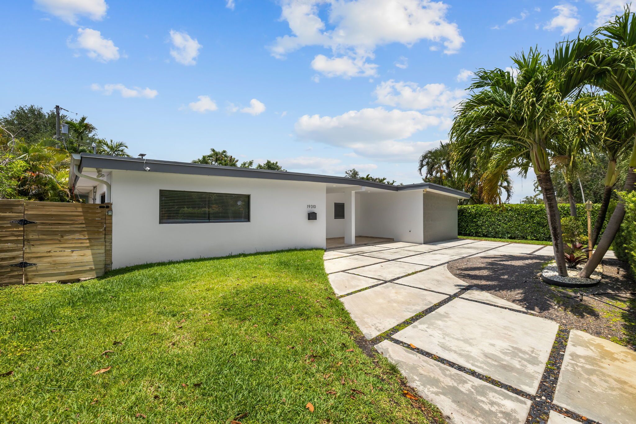 Une maison moderne à l’extérieur blanc, avec une allée pavée et une pelouse bien entretenue.