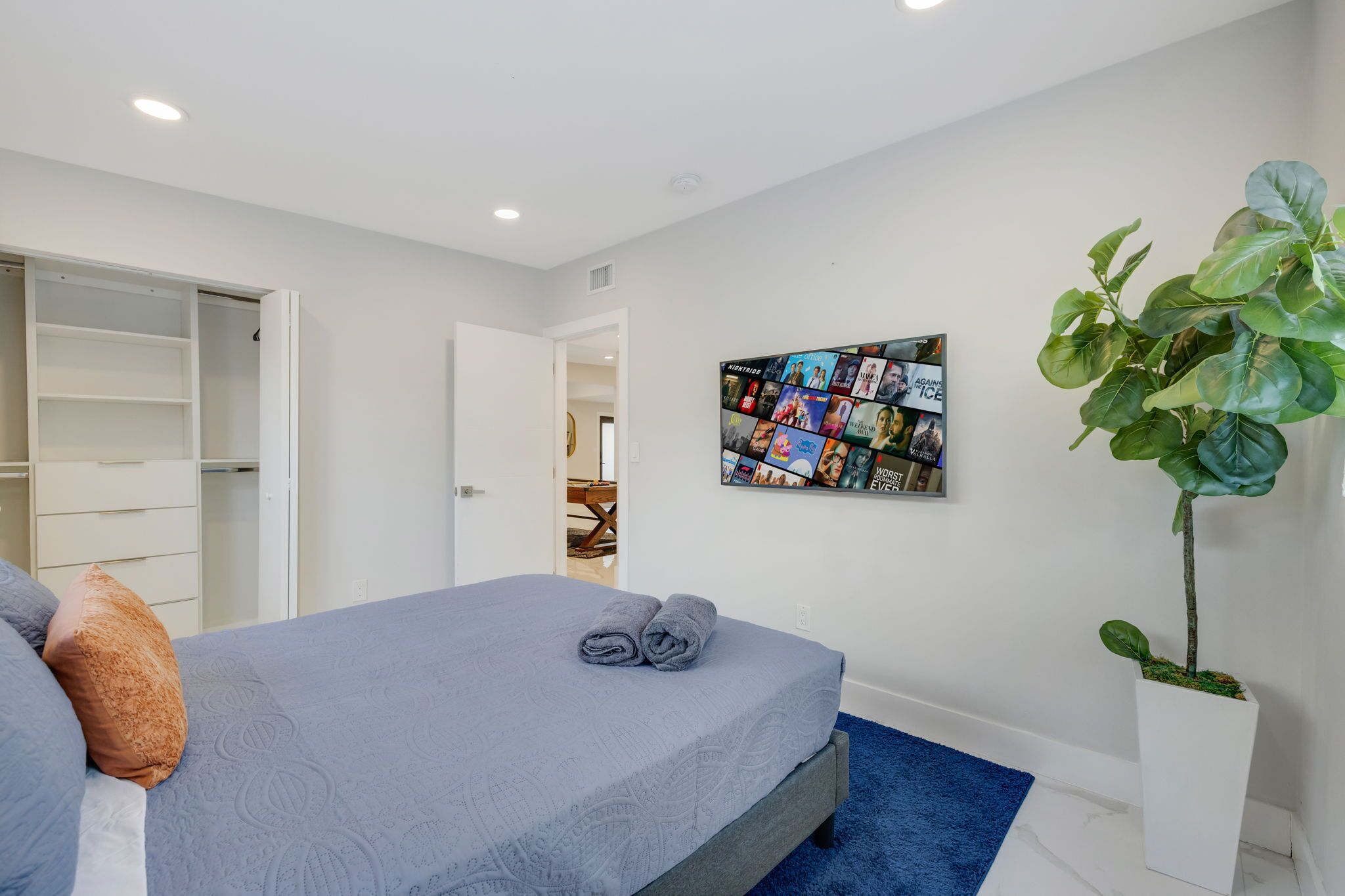 A bedroom with a bed, a wall art piece, a potted plant, and a closet.