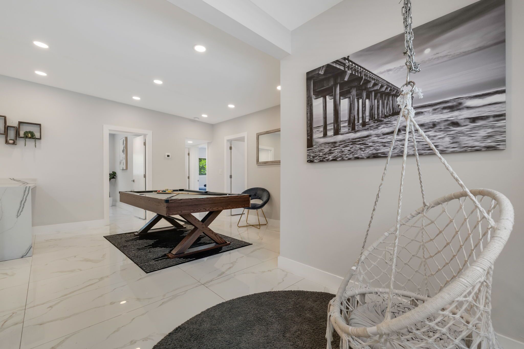 A modern interior with a pool table, a hanging chair, and a painting of a pier.