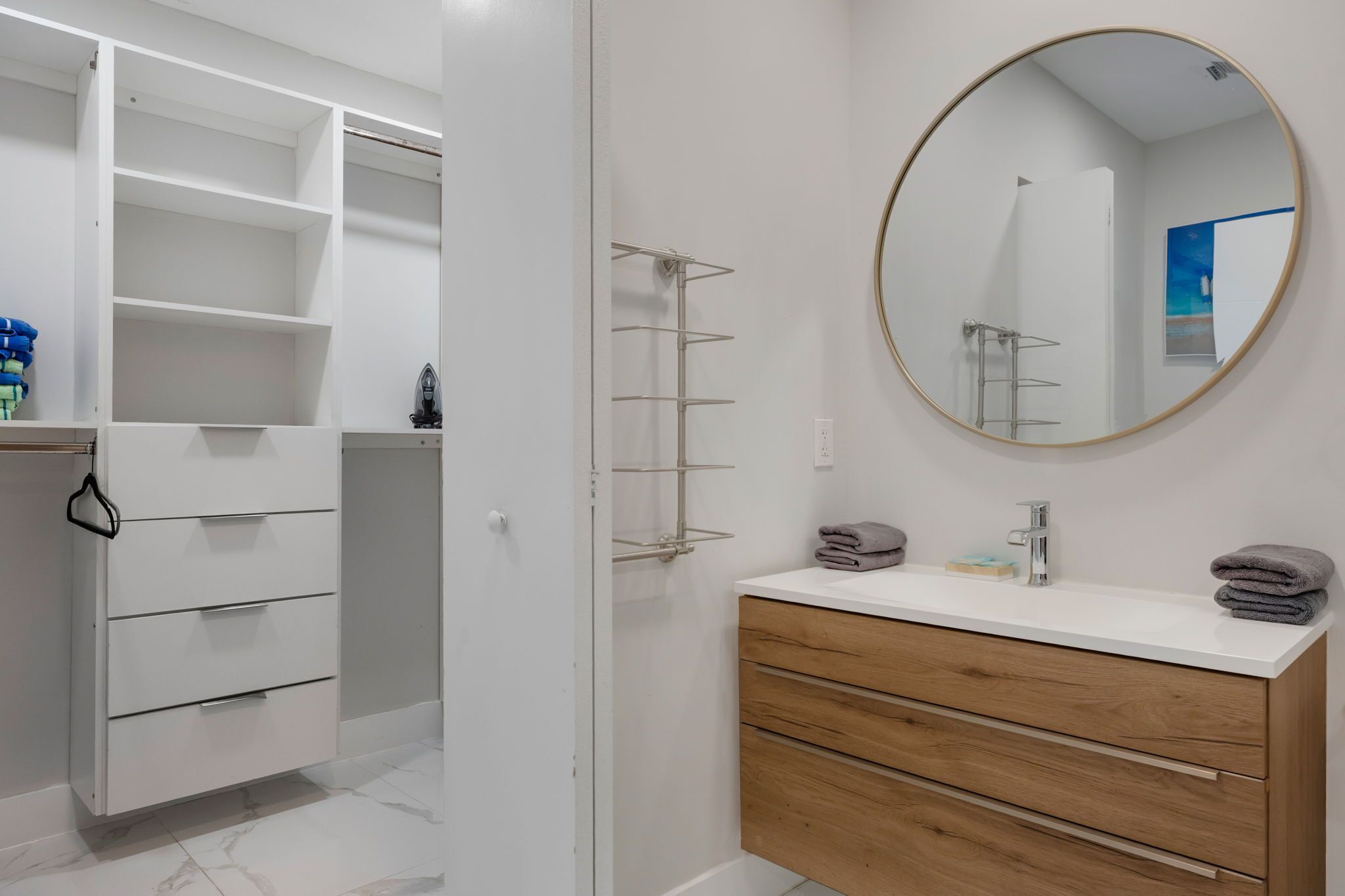 A modern bathroom with a white vanity, a round mirror, and a built-in shelving unit.