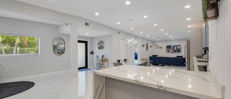 A spacious kitchen with a marble countertop, recessed ceiling lights, and a view of the dining area.