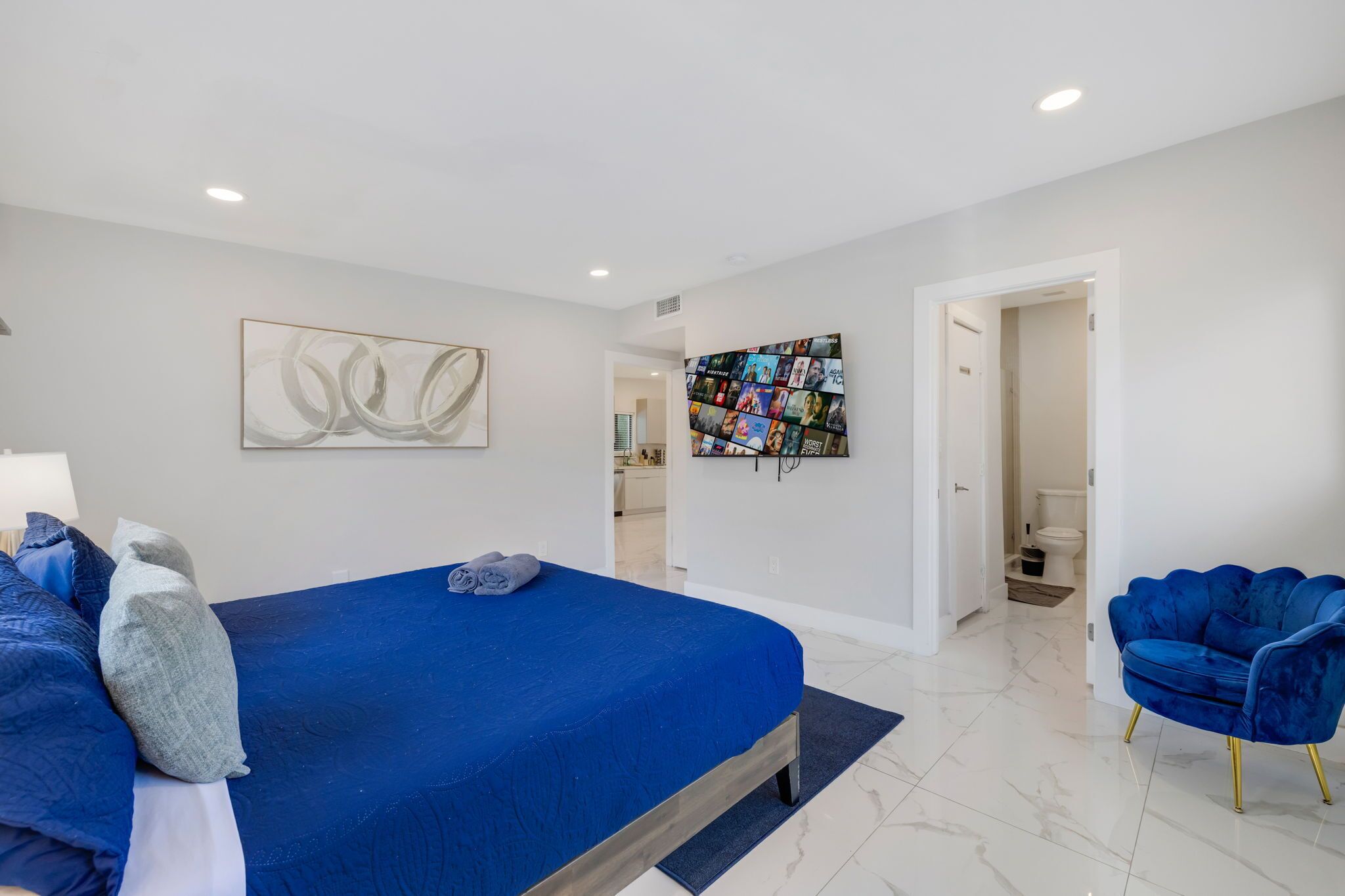 Un dormitorio moderno con una cama grande, una silla azul y una obra de arte en la pared.