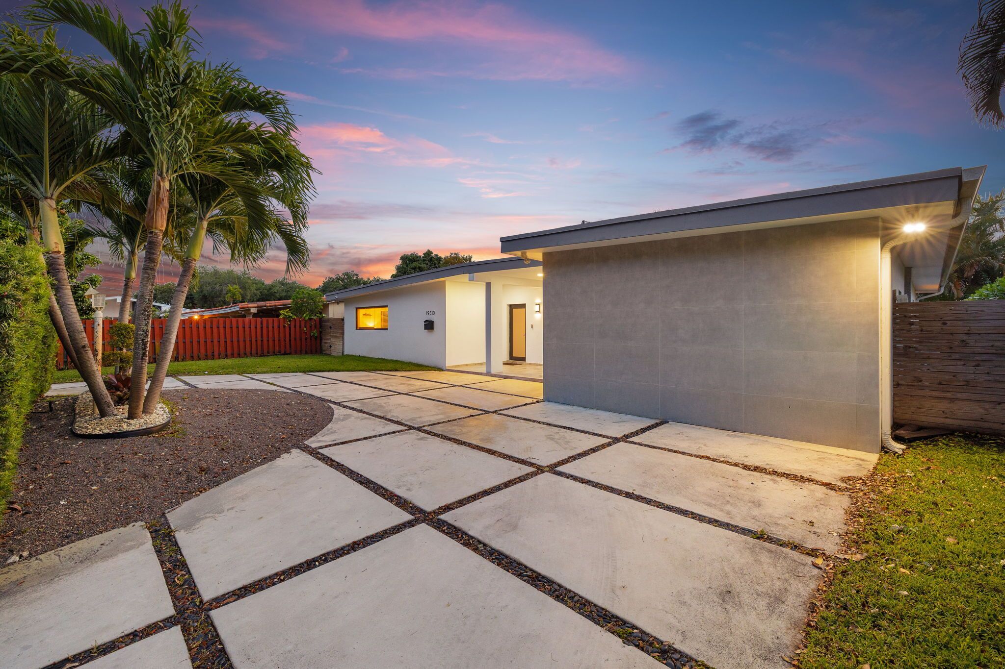 Una casa moderna con fachada de hormigón, camino de entrada pavimentado y valla roja.