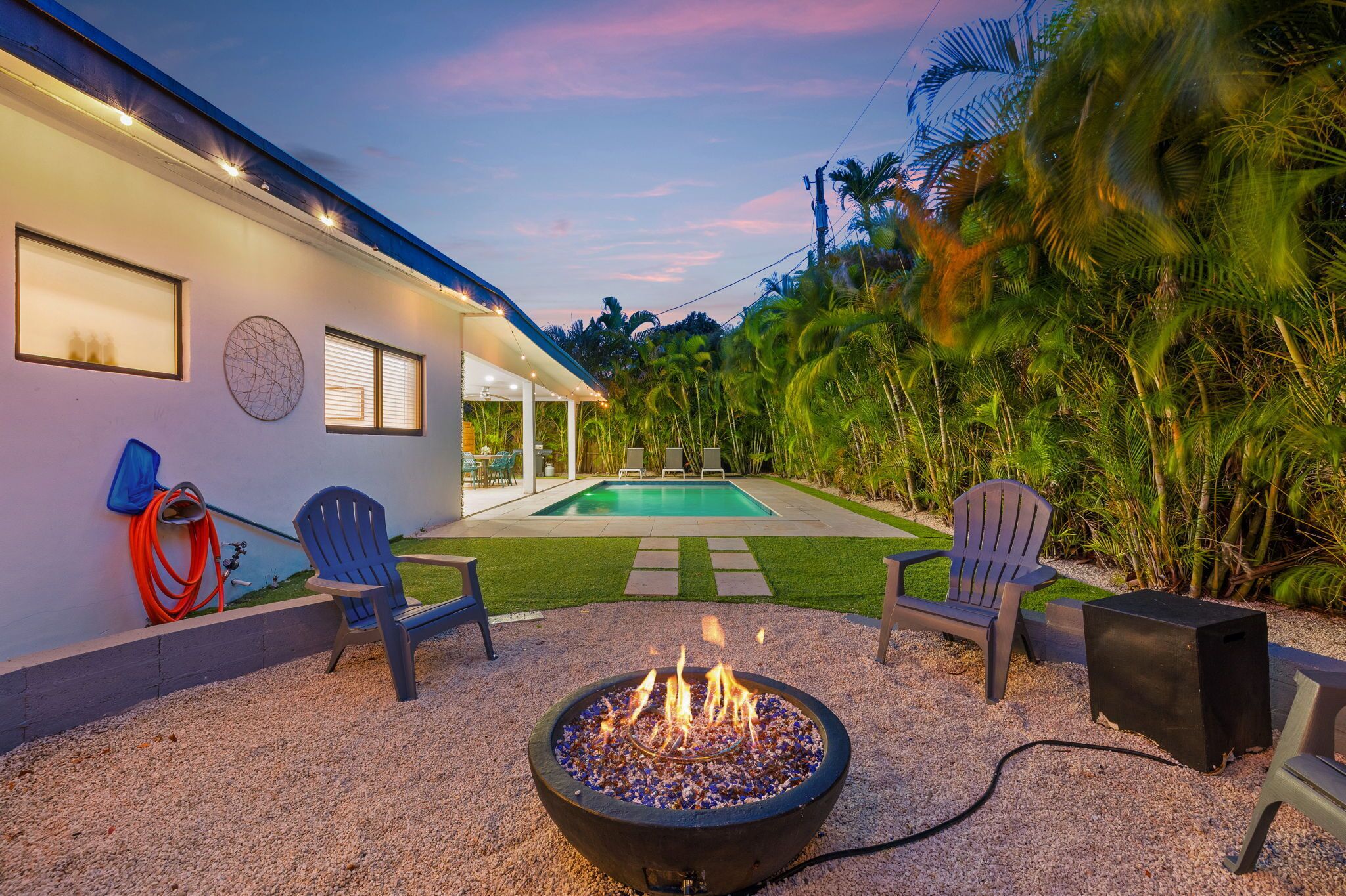 A backyard with a fire pit, outdoor seating, a pool, and a house with a modern design.