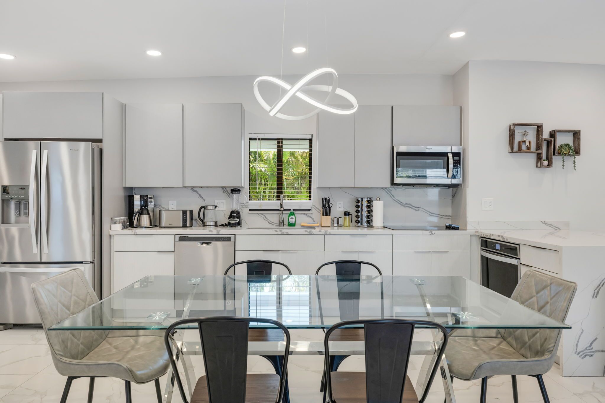 A modern kitchen with stainless steel appliances, a glass dining table, and a unique ceiling light.