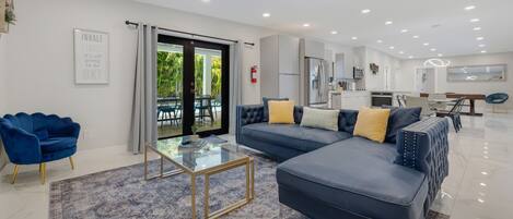 A modern living room with a sofa, a glass coffee table, and a blue armchair.