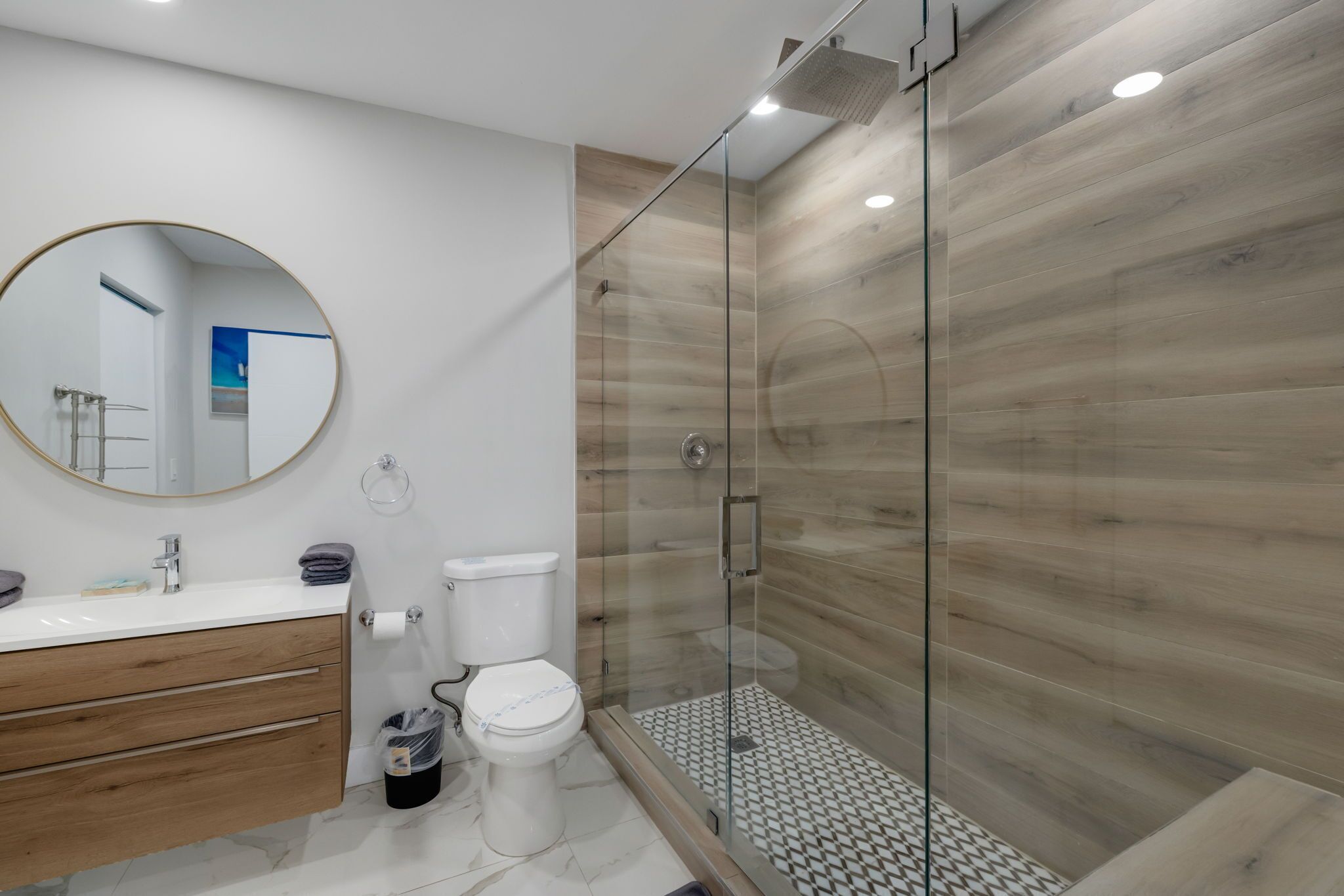 A modern bathroom with a glass-enclosed shower, a round mirror, and a wooden vanity.