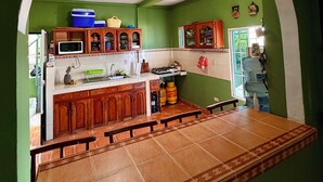 Une cuisine avec des murs verts, des meubles en bois, un sol carrelé et un grand distributeur d’eau.