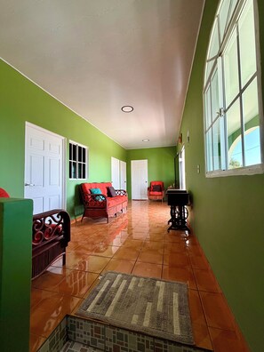 A hallway with green walls, white doors, and a tiled floor. There is a red sofa with cushions and a small table with a lamp.