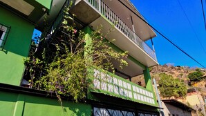 Un immeuble de deux étages avec une façade verte, un balcon doté de balustrades blanches et un garage avec un portail noir.
