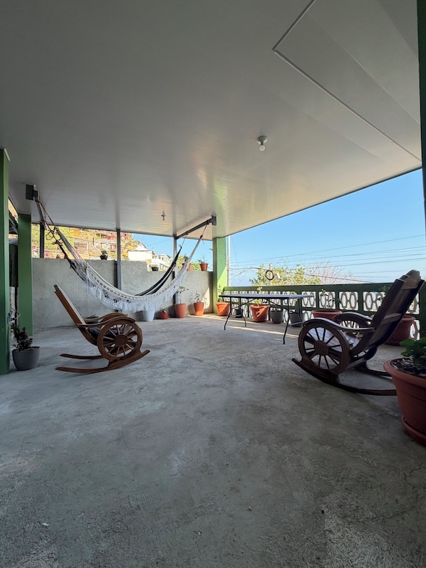 A covered outdoor area with a hammock, rocking chairs, and potted plants.