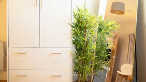 Une pièce avec une armoire blanche, une plante en pot, un miroir et une lampe.
