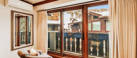 Una habitación con un gran ventanal corredero que da a un balcón, una silla y una mesita.