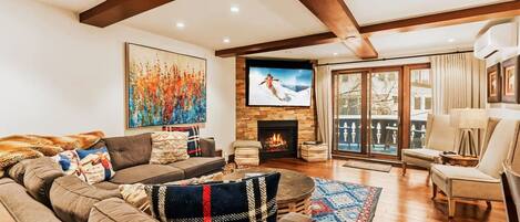 A cozy living room with a fireplace, a large TV, and a view of the outdoors.