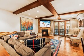 A cozy living room with a fireplace, a large TV, and a view of the outdoors. - Vail Village 5BR, Sleeps Ten (Vail)
