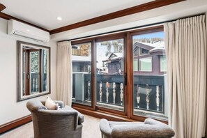 A room with a large sliding glass door leading to a balcony, a chair, and a small table. - Iconic Vail Village Retreat | Walk to Everything! (Vail)