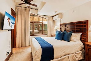 Une chambre d’hôtel équipée d’un lit, d’une télévision, d’un ventilateur de plafond, d’une fenêtre avec des rideaux et d’un appareil de climatisation.
