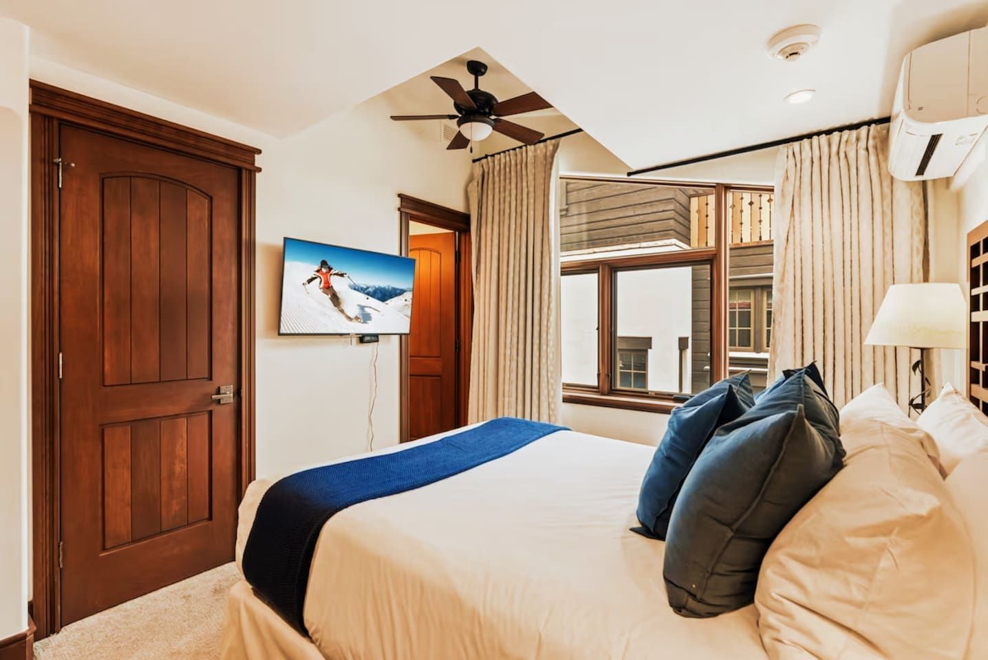 A hotel room with a large bed, a ceiling fan, a television mounted on the wall, and a window with curtains.