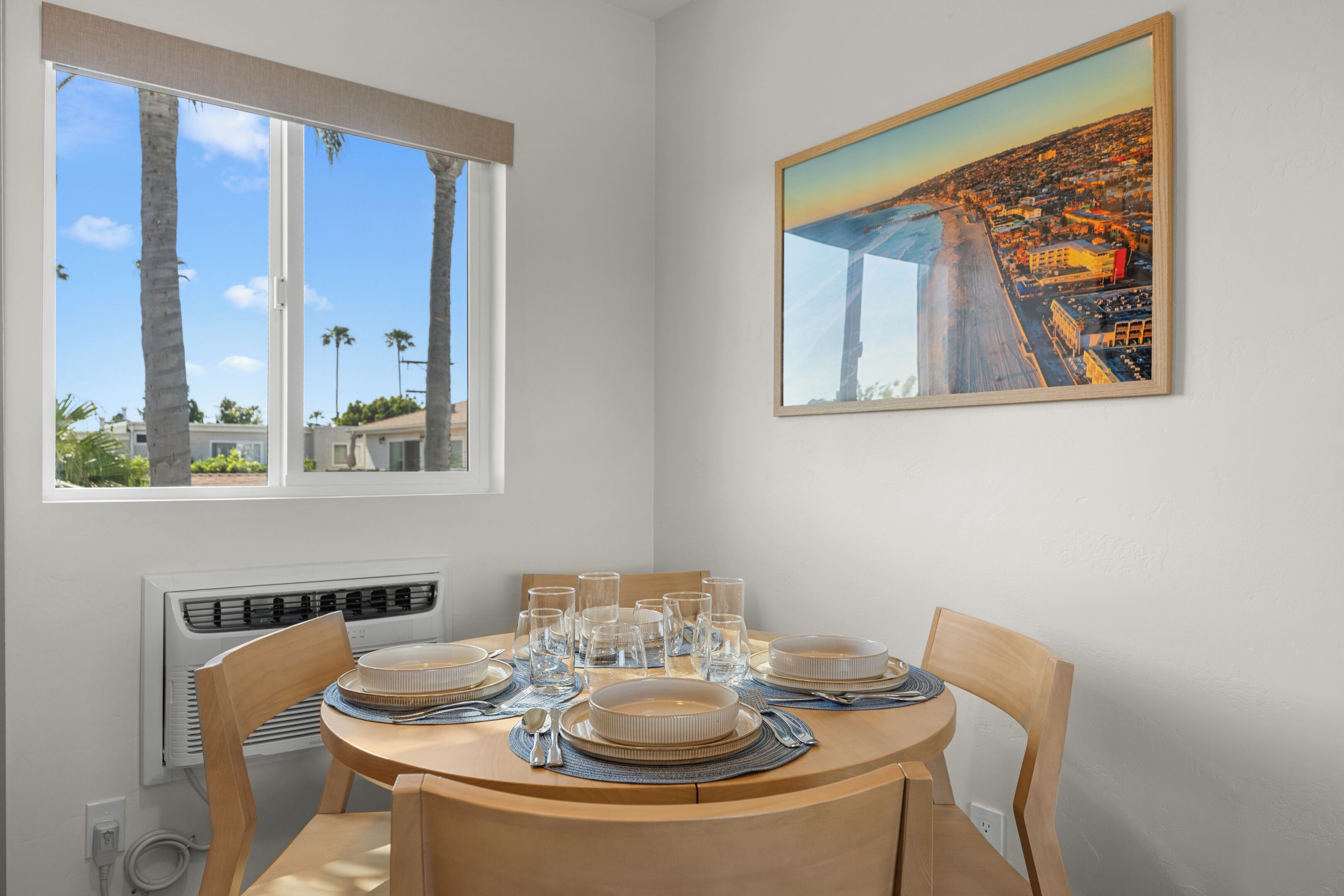 A dining area with a round table, chairs, and a painting of a coastal cityscape.