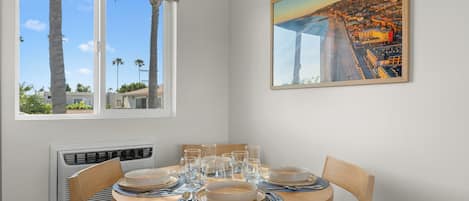 A dining area with a round table, chairs, and a painting of a coastal cityscape.