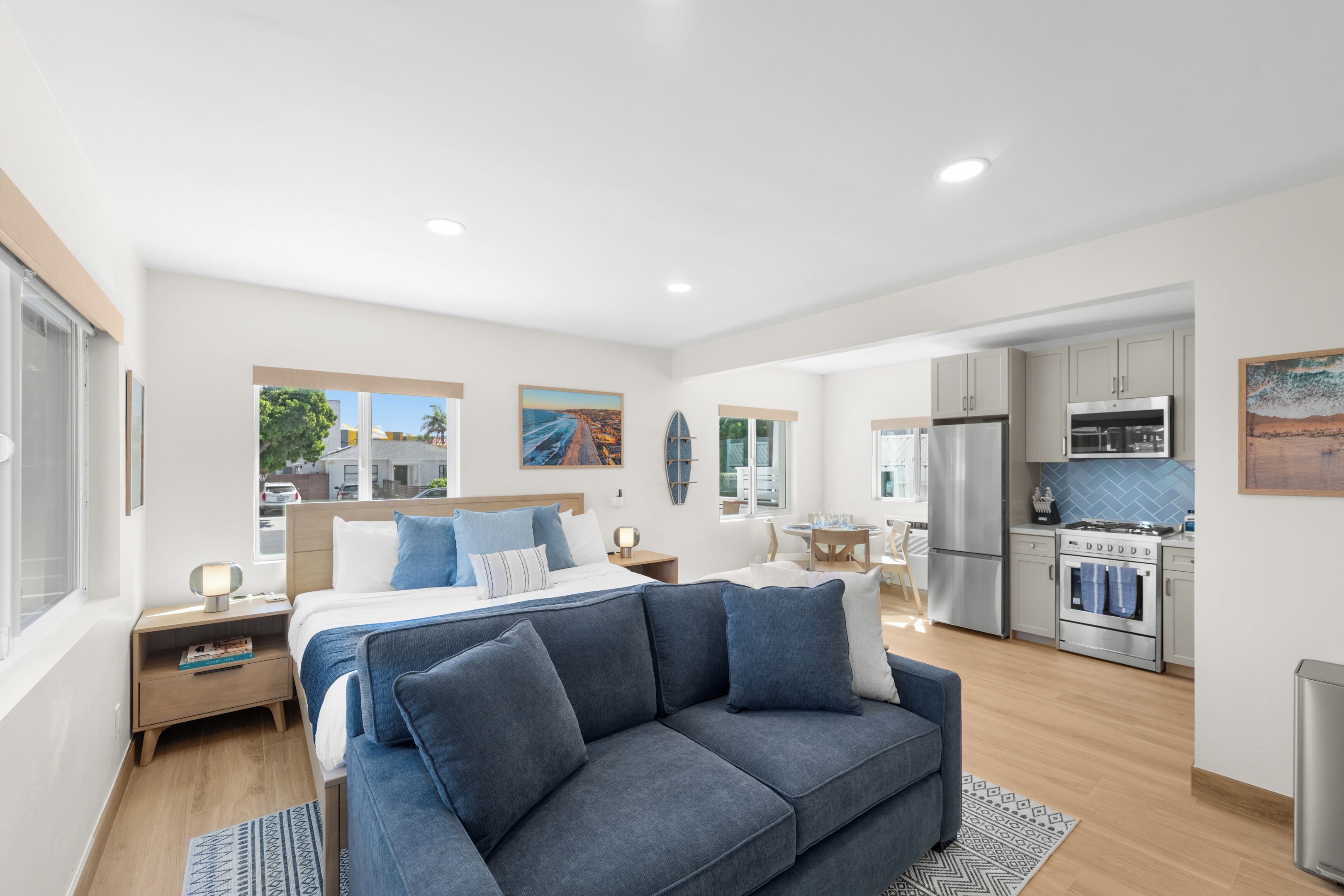 A modern bedroom with a bed, a blue sofa, a kitchen with appliances, and a dining area.