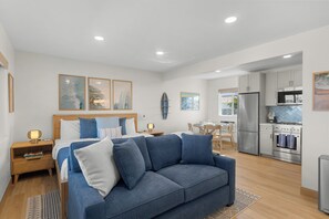A modern hotel room with a bed, a blue sofa, a dining area, and a kitchen. - Pacific Tides -Entire 9-Unit Apartment Complex w/ Parking + A/C in Pacific Beach (San Diego)