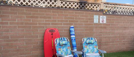 A wall with a brick pattern, two beach chairs, a red surfboard, and two signs indicating quiet hours and no poop/pee zone.